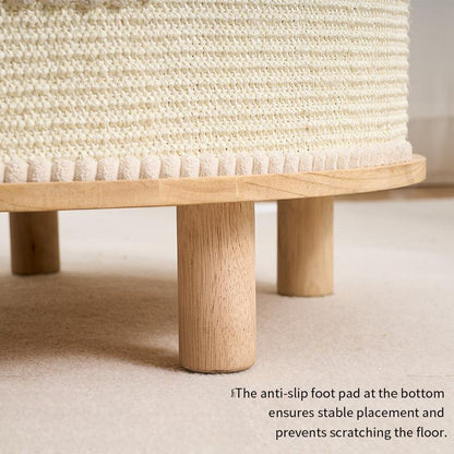 Close-up of a woven off-white textured ottoman or cat house with light natural wood legs on a beige carpet, with a small text note at the bottom right.
