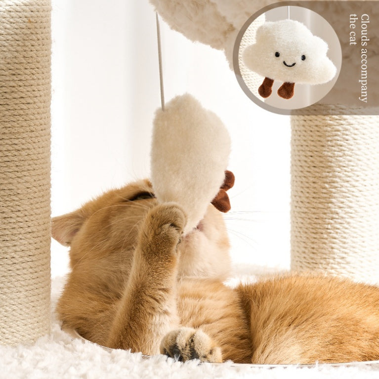 A cat playing with a cloud-shaped toy lying on a white cat bed in a white sisal cat tree.