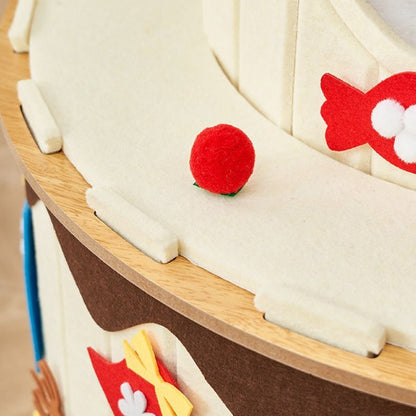 Close-up of a wooden cat condo with cream-colored felt sails, brown hull details, and small red felt fish accents, with a small red ball on the deck.