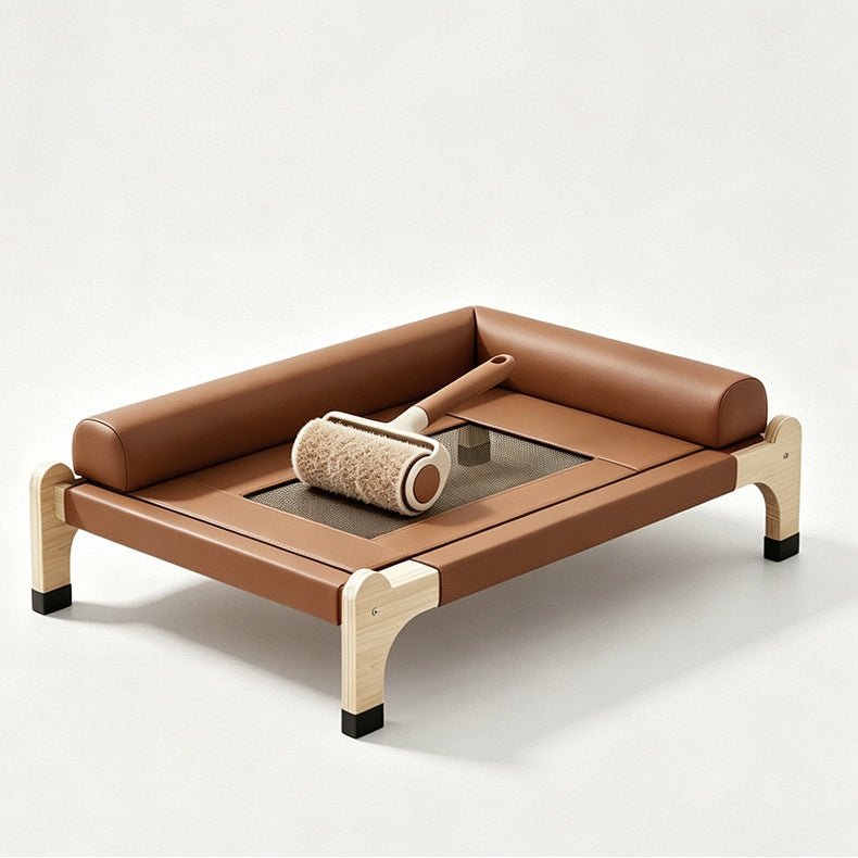 A brown leather elevated cat bed with a low rectangular frame, light wood legs, and black feet, shown on a clean, light gray studio background. A grooming roller rests on the bed.