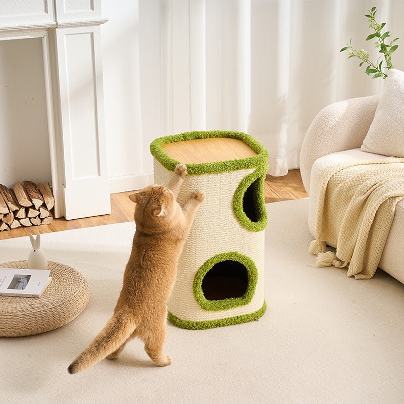 A ginger cat stands on its hind legs, reaching up to a tall, large cat tower in a bright, modern living room. The cat tree has a cream-colored woven body with green grass-textured trim and two openings, one on each side.