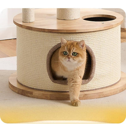 A round and large cat tree with a sisal-wrapped condo, sturdy top and base, and a circular opening where a ginger cat is peeking out, photographed indoors on a light floor.