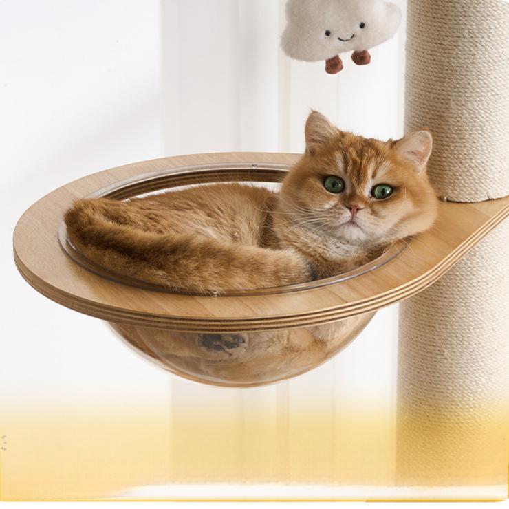 An orange large-breed cat rests inside a wooden cat tower with a clear bowl, attached to a sisal scratching post. A small white plush cloud toy hangs above.
