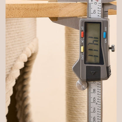 A digital caliper measuring a wooden board, with a blurred woven textile in the background. The caliper is gray with a digital LCD screen showing measurements.