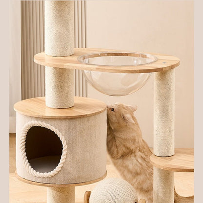 A multi-level cat tree with light wood, firm platforms, beige sisal-wrapped posts, a clear glass hanging bowl, and a round cat house, shown with a ginger cat climbing and using the tree in a warm indoor setting.