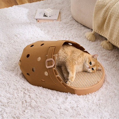 A fluffy orange fat cat lies inside a brown shoe-shaped cat bed with a scratching pad on the bottom, placed on a white shag rug in a cozy room setting.